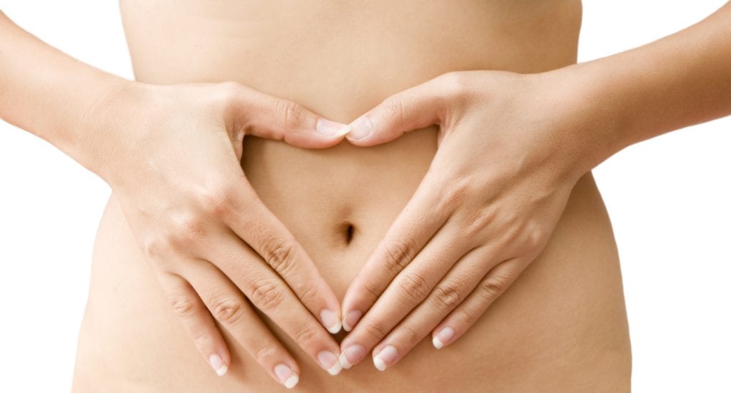 A woman's hands forming a heart symbol on belly